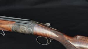 Fusil de chasse T. GICQUEL, juxtaposé, crosse en bois gravée, boîtier de culasse en acier orné de motifs floraux. Détail du levier de déverrouillage.