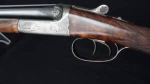 Fusil de chasse TONY GICQUEL à double détente, boîtier gravé de canards en vol et volutes, crosse en noyer finement quadrillée.