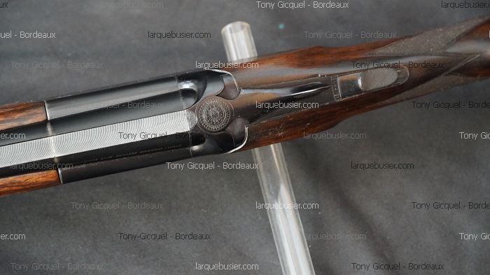 Boîtier de culasse et canons d'un fusil de chasse juxtaposé, gravure circulaire détaillée, levier d'ouverture texturé.