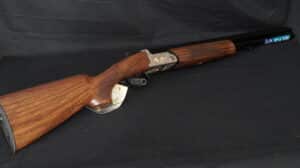 Fusil de chasse superposé FAIR en bois veiné et métal. Culasse gravée d'oiseaux dorés. Étiquette: «GARANTIE 10 ANS» visible.