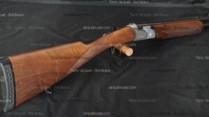 Fusil de chasse superposé avec crosse en bois et bascule argentée gravée, sur fond noir. Textes : Tony Gicquel - Bordeaux, larquebusier.com.