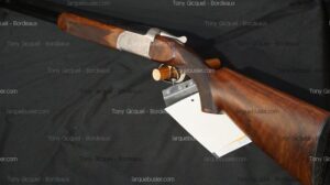 Fusil superposé en bois de noyer veiné et bascule argentée. Détente dorée, mécanisme de sécurité. Article de chasse ou sport.