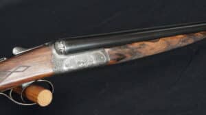 Fusil de chasse superposé T. GICQUEL, crosse bois gravée, bascule argentée ornée de motifs floraux et deux canards en vol.