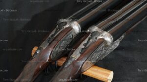 Paire de fusils de chasse artisanaux numérotés 1 et 2, avec gravures détaillées sur la platine et crosse en bois. Levier de sûreté indiquant 'SAFE'.