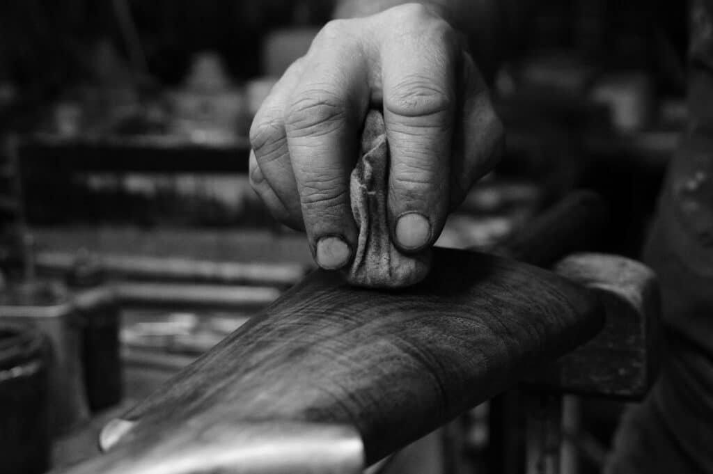 Main d'artisan avec un chiffon polissant méticuleusement la crosse en bois d'un fusil, mettant en valeur son grain.