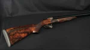Fusil superposé élégant avec crosse en ronce de noyer foncé et récepteur en acier ouvragé, sur fond noir uni.